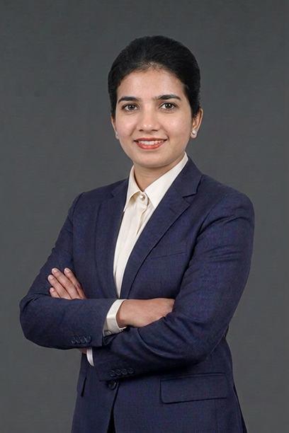 Professional portrait of a woman in a navy blazer and white shirt with arms crossed against a gray background.