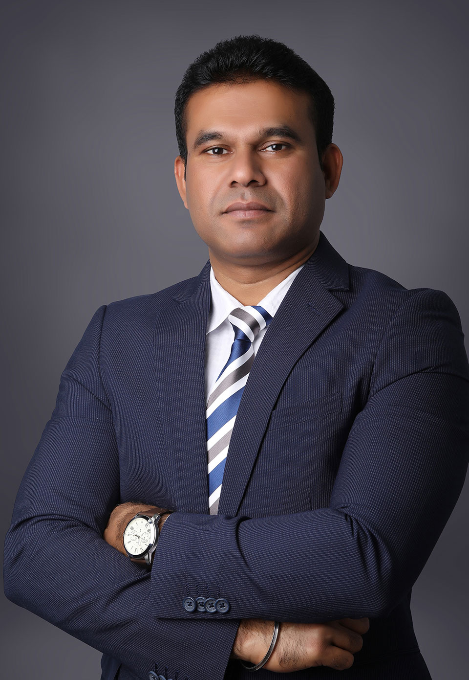 Professional head-and-shoulders portrait of a man in a navy pinstripe suit with a striped tie, arms crossed against a gray background